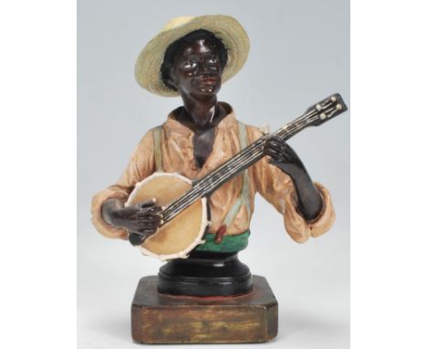 A 19th Century Austrian cold painted ceramic figurine depicting a black man playing the banjo supported on a square plinth ba