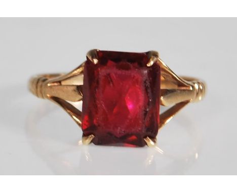 A marked 9ct yellow gold ring having a square cut red stone set to a decorative pierced mount with ribbed shoulders. Marked 9