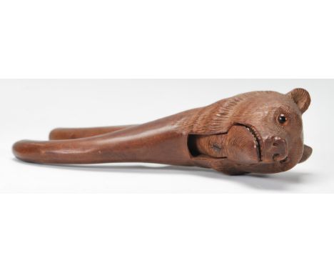 An early 20th Century black forest wooden nut cracker in the form of a bear having carved detailing set with glass eyes. Insc