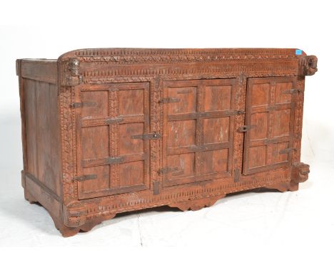 A 20th Century hardwood cupboard chest of Indian origin, carved profusely&nbsp; to the front with three panel doors, metal ca