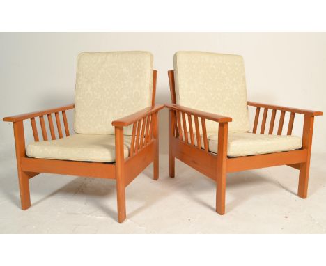 A pair of 20th Century vintage retro teak wood framed lounge arm chairs having a slatted backrest and arm supports with white