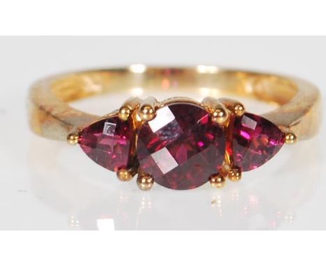 A 9ct gold (stamped 9k) Rhodolite garnet three stone dress ring, the ring set with central faceted cut rhodolite stone flanke