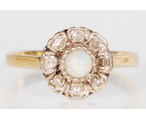 A stamped 18ct gold ladies ring having a flower head set with a central round opal with white stone accent stones surrounding