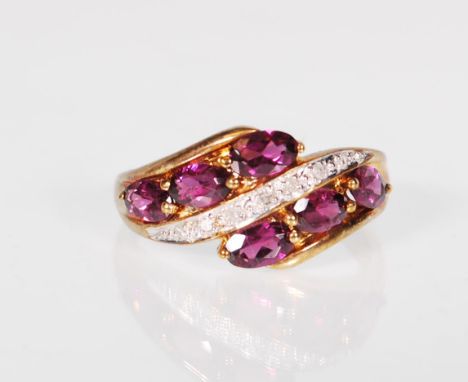 A 9ct gold hallmarked garnet and diamond cross over dress ring, central line of diamonds flanked by six garnet set stones. Si