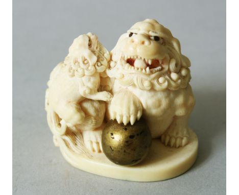 A JAPANESE MEIJI PERIOD CARVED IVORY NETSUKE OF SHI SHI DOGS, the larger shi shi with its paw upon a revolving gilded ball, t