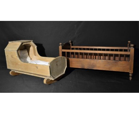 AN early 20th century stained pine dolls cot bed, 62cm long;  a smaller pine rocking cradle, with mattress and pillow, 50cm l