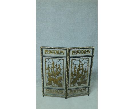 An antique painted firescreen with pierced brass panels with strung floral and foliate design and repeating leaf motif border