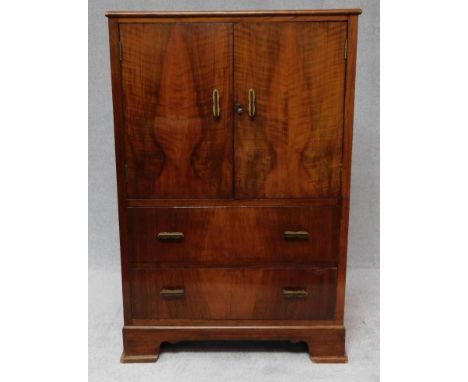A mid century figured walnut cabinet with a pair of panel doors above drawers on bracket feet. H.110 W.73 D.43cm 