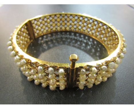A gold bangle with open wirework set with grey freshwater pearls, unmarked, one pearl missing