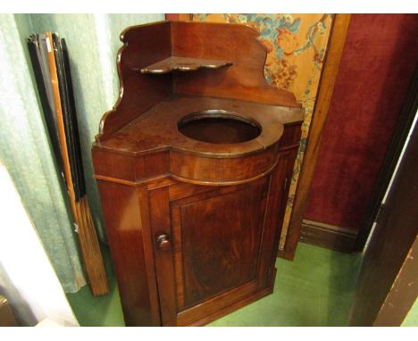 An early Victorian flame mahogany corner washstand, the raised back over a ceramic wash bowl insert and single door cupboard,