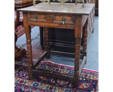 A late 17th/18th century oak side table, the frieze drawer with applied moulded panels and drop brass pulls, raised on bobbin