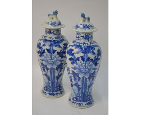 A pair of Chinese blue and white vases; each one with a domed cover and Buddhist Lion dog finial,  decorated with bold floral