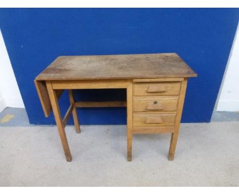 An early 20th Century light oak single pedestal desk of three drawers with single drop flap to one end.