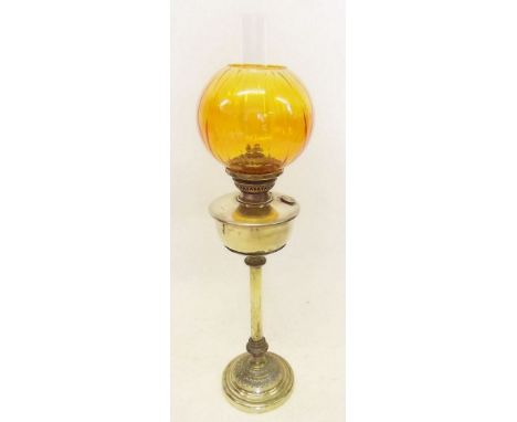 A brass oil lamp with orange glass shade