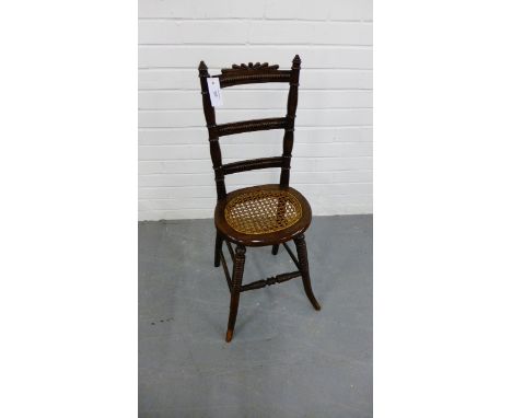 A 19th century mahogany child's correction chair, having a carved top rail over ladder back and cane work seat raised on turn