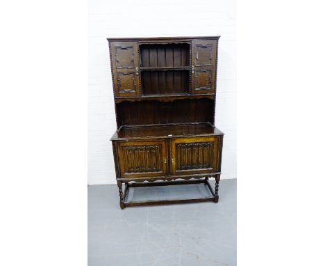 A vintage oak kitchen dresser, having a moulded cornice over central shelf flanked by panel doored cabinets, above two carved