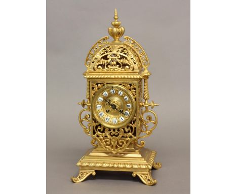 A VICTORIAN GILT BRASS MANTEL CLOCK. The elaborate pierced scrolling case containing a central dial with enamelled Roman nume