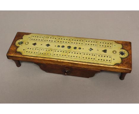 A LATE VICTORIAN OAK AND BRASS CRIBBAGE BOARD. The rectangular oak top mounted with a brass cribbage board pierced with heart
