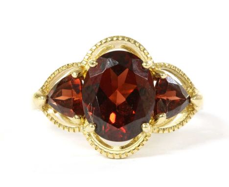 A 9ct gold three stone garnet ring, with an oval mixed cut garnet with a triangular mixed cut garnet at each side, to openwor