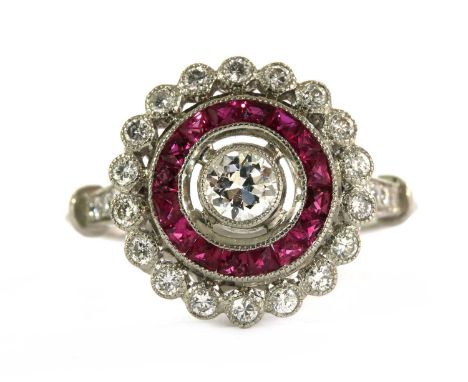 A diamond and ruby target cluster ring. with a brilliant cut diamond milligrain set at the centre, to surround of calibré Fre