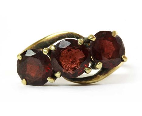 A gold three stone garnet crossover ring, with a row of circular mixed cut garnets, approximately 7mm, claw set to crossover 