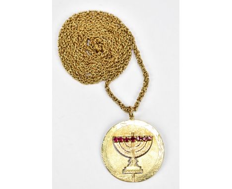A yellow metal circular pendant inscribed 'Israel' and featuring swivel menorah set with blue and red stones to either side, 