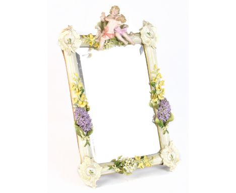 A circa 1900 Continental porcelain mirror, surmounted with two cherubic figures and decorated with floral sprays with wooden 