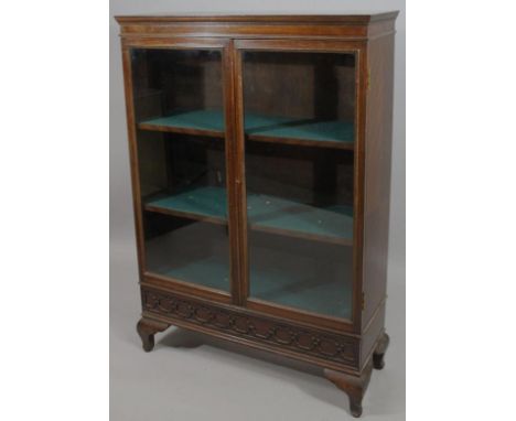 A mid-20thC oak display cabinet, with a quarter veneered top raised above two glazed doors above a blind fret panel on compre