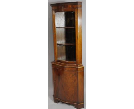 A 20thC walnut and mahogany corner display cabinet, of serpentine outline, the upper section with a dentil top raised above a