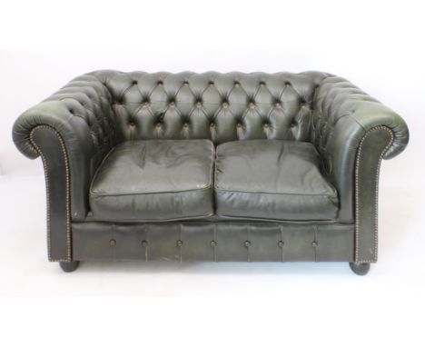 A green leather two-seater Chesterfield sofa - raised on four bun feet (LWH 148 x 87 x 71 cm)