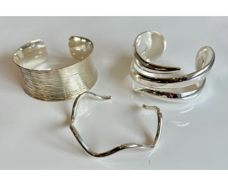 Three modernist sterling silver bangles - each stamped 925, comprising a bark effect cuff bangle, a pierced spiral cuff bangl