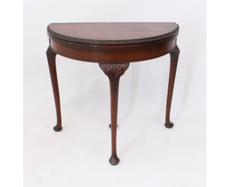A 1920s-30s mahogany demi-lune card table - the fold over top with foliate carved edge and green baize, opening on a pull-out