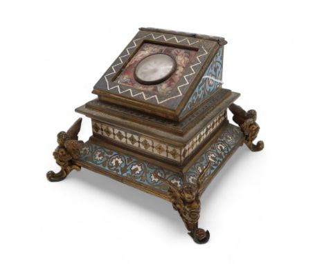A FRENCH CHAMPLEVE ENAMEL INKWELL the lid inset with a small clock within an enamel panel depicting angels and cupids, upon f