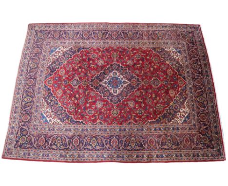 A RED GROUND IRANIAN TRADITIONAL KASHAN CARPET&nbsp; with dark blue and cream diamond central medallion and matching spandrel