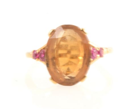 A Citrine dress ring, the oval mixed cut stone 14mm x 10.5mm four claw set in a yellow metal mount with two rubies set into e