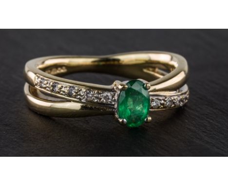 A 9ct yellow gold, emerald and diamond ring, the oval cut emerald within a split shank half-set with small diamonds, ring siz