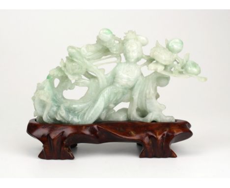 A Chinese pale mottled jade figure, late 20th century, the semi-recumbent figure of Guanyin dressed in robes, amidst peaches 