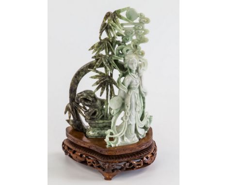 A pale green to mottled grey Chinese carved jade figure, late 20th century, depicting Guanyin in fine flowing robes before a 