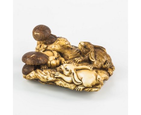 A Japanese carved ivory netsuke, Meiji period (1868-1912), with three leverets playing amongst toadstools, on naturalisticall