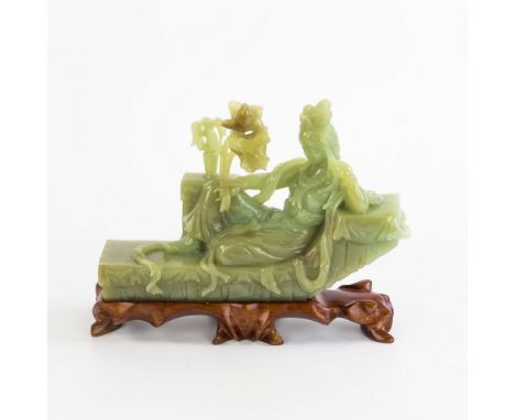 A Chinese celadon green carved jade figure, late 20th century, the jade with some brown inclusions, modelled as a female recl