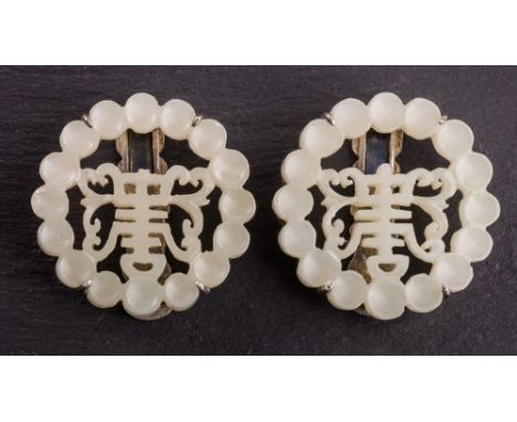 A pair of Chinese carved pale celadon jade and silver shoe or collar clips, early 20th century, the jade with pierced calligr