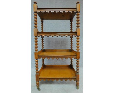 A Victorian honey oak four tier buffet on turned tapering supports terminating in brass cup casters. H.122 W.62 D.44cm 