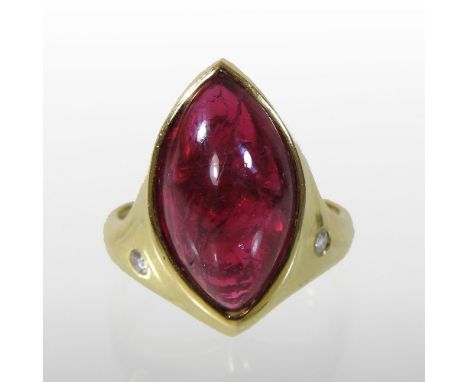 An 18 carat gold, polished ruby coloured and diamond ring, set with an elliptical uncut stone, flanked by a pair of diamonds,