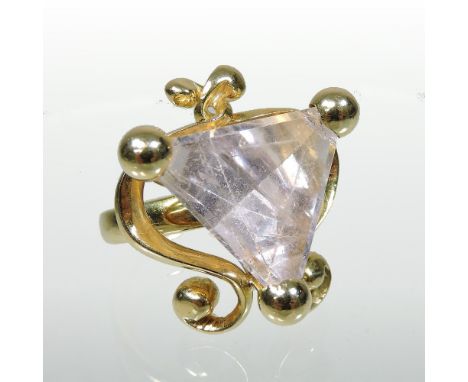 A modern 18 carat gold and quartz set ring, set with a large triangular pink stone, within a scrolled openwork surround, stam