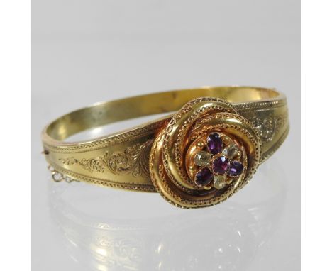 An ornate unmarked gilt bangle, of hinged design, finely engraved with scrolling foliate designs, centred by a filigree decor