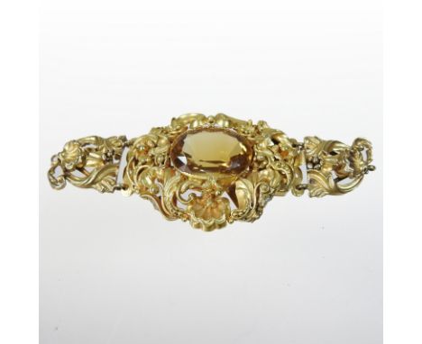 An ornate gilt stomacher, inset with a central oval citrine, within a profusely scrolled surround, decorated with shells, scr