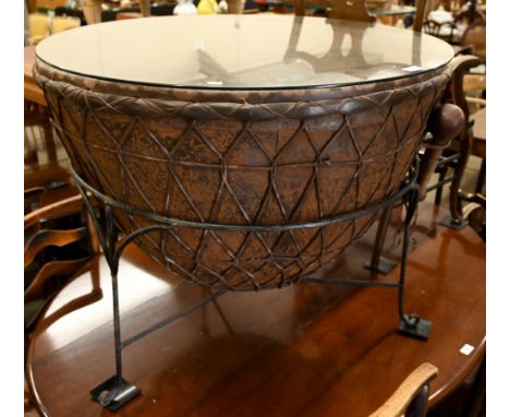 An ethnic kettle drum with glass top - as a coffee table - on wrought iron frame base, 89 cm dia., c/w two mallet drumsticks