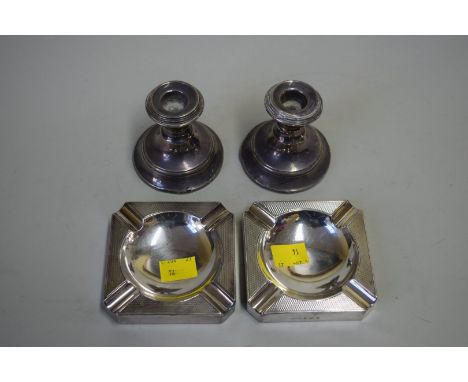 A pair of silver ashtrays, by BMC Ltd, having engine turned decoration; and a pair of squat silver candlesticks.