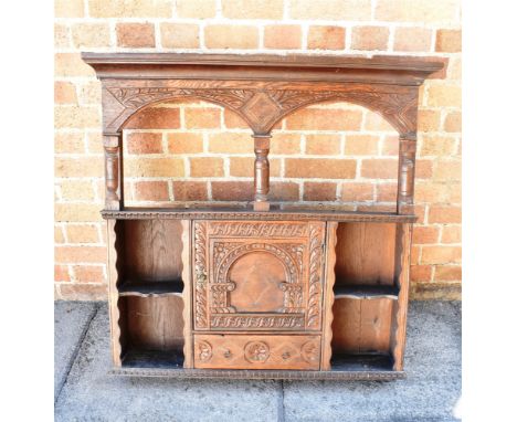 A CARVED OAK OVERMANTEL  with a shaped cornice and twin shallow arches over an open shelf, above a central cupboard and a sin