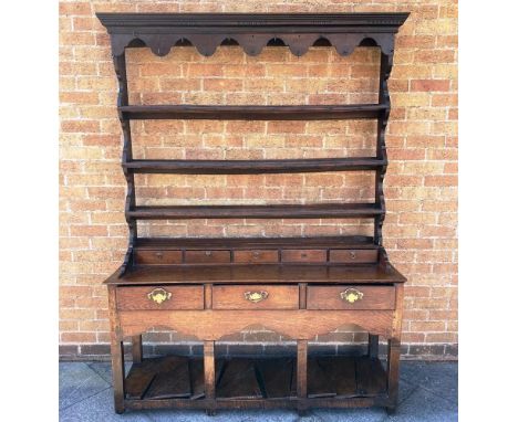 AN OAK DRESSER  the rack with moulded cornice and shaped apron, three shelves and five spice drawers, the base with three dra